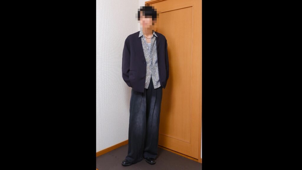 濃い色のジャケットに豹柄のシャツ、黒のワイドパンツと黒の革靴を合わせた着こなし